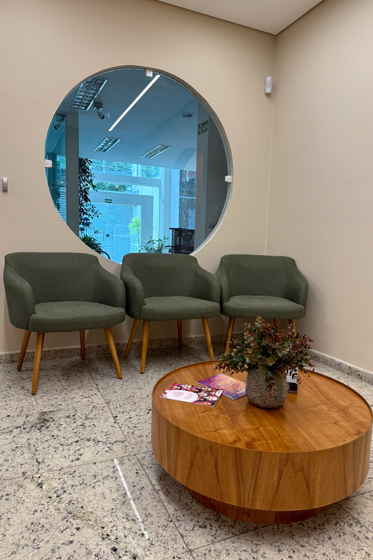 Recepção com três poltronas verdes e mesa de centro de madeira